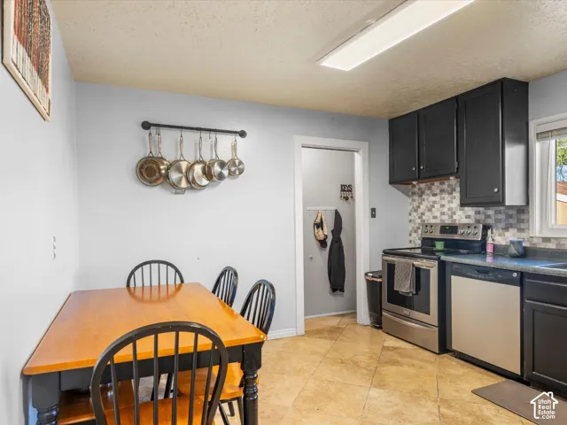 Kitchen featuring black cabinetry, stainless steel appliances, mosaic tile backsplash, and tile flooring