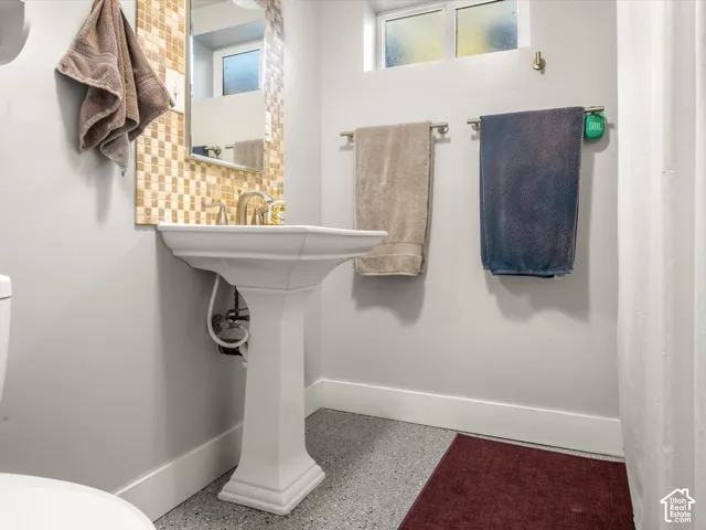 Pedestal sink with a brushed nickel faucet, mosaic tile backsplash, and light gray walls