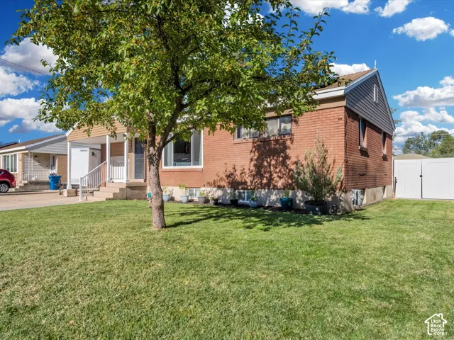 Brick exterior with vinyl siding accents, mature front yard tree, concrete front steps with railings, and a white privacy fence