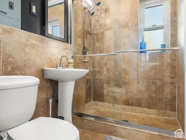 Pedestal sink, wall-mounted mirror, tiled shower enclosure with glass sliding door, and a window