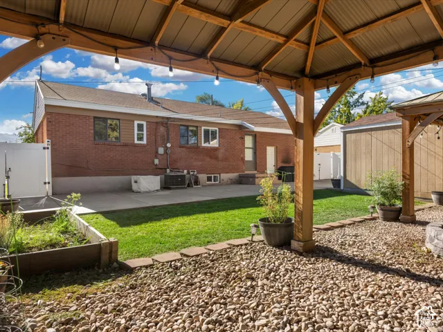 Wooden gazebo with string lighting, pea gravel ground cover, concrete patio, and fenced yard
