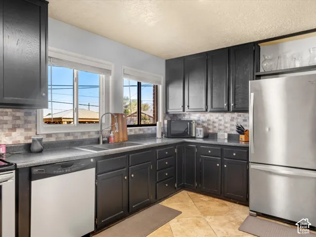 Kitchen featuring dark wood-finish cabinetry, tile backsplash, laminate countertops, and stainless steel appliances