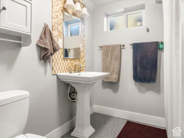Pedestal sink with brass-finish faucet, mosaic tile backsplash, and overhead lighting