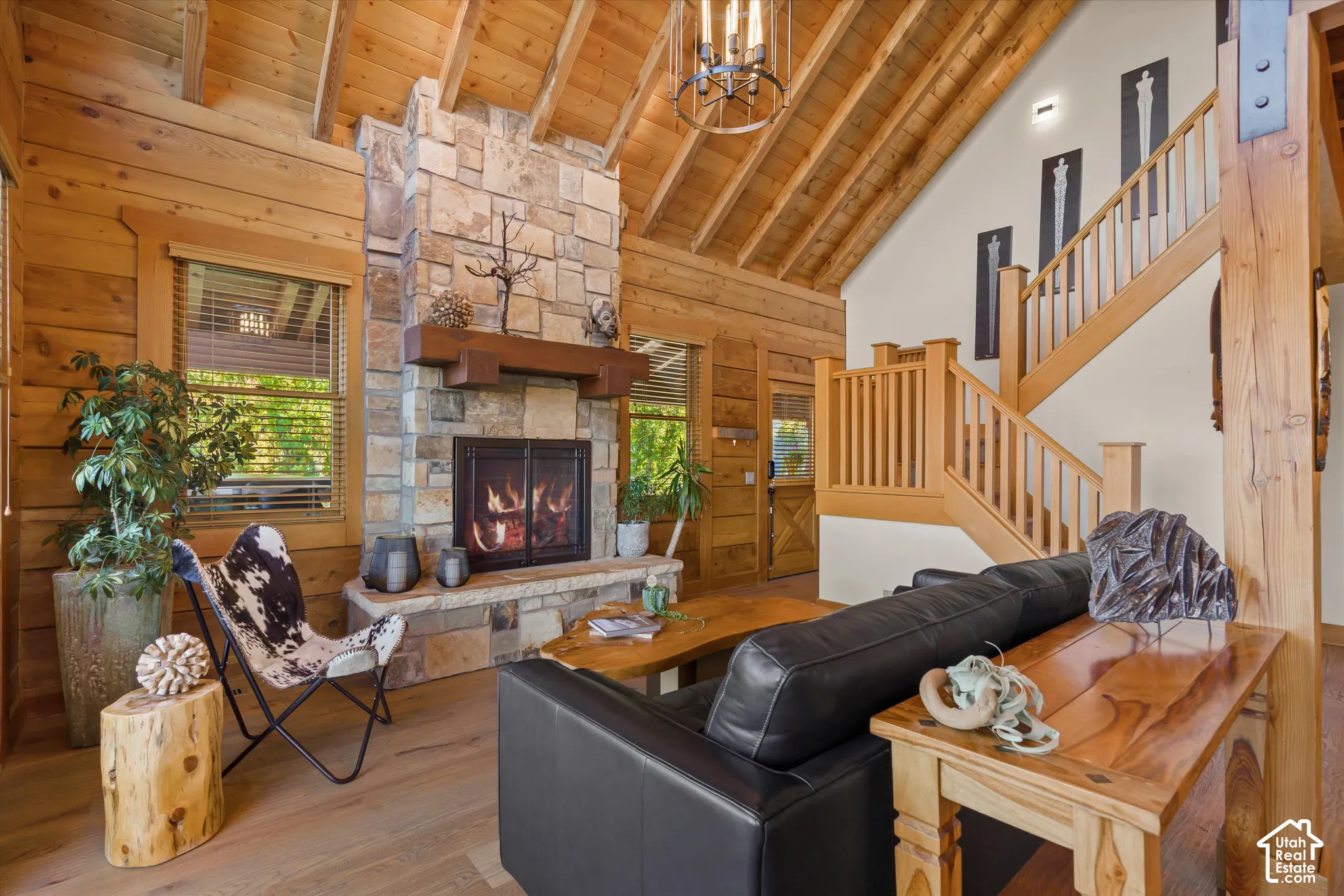 Vaulted wood-finish ceiling, stone-clad fireplace with mantel, exposed wood beams, wood-finish flooring, and a natural wood staircase