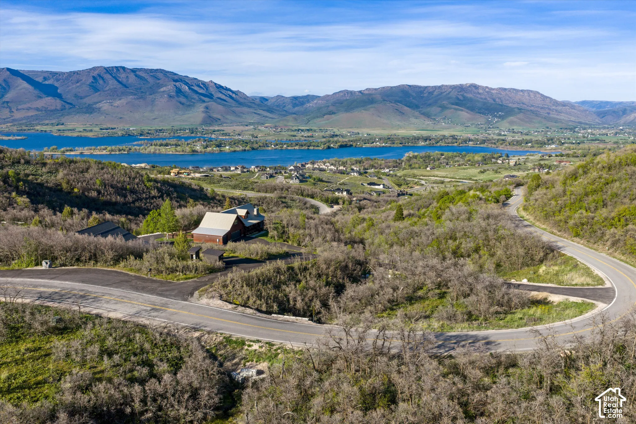 Expansive natural surroundings with a winding paved roadway, a distant lake, and mountain range backdrop