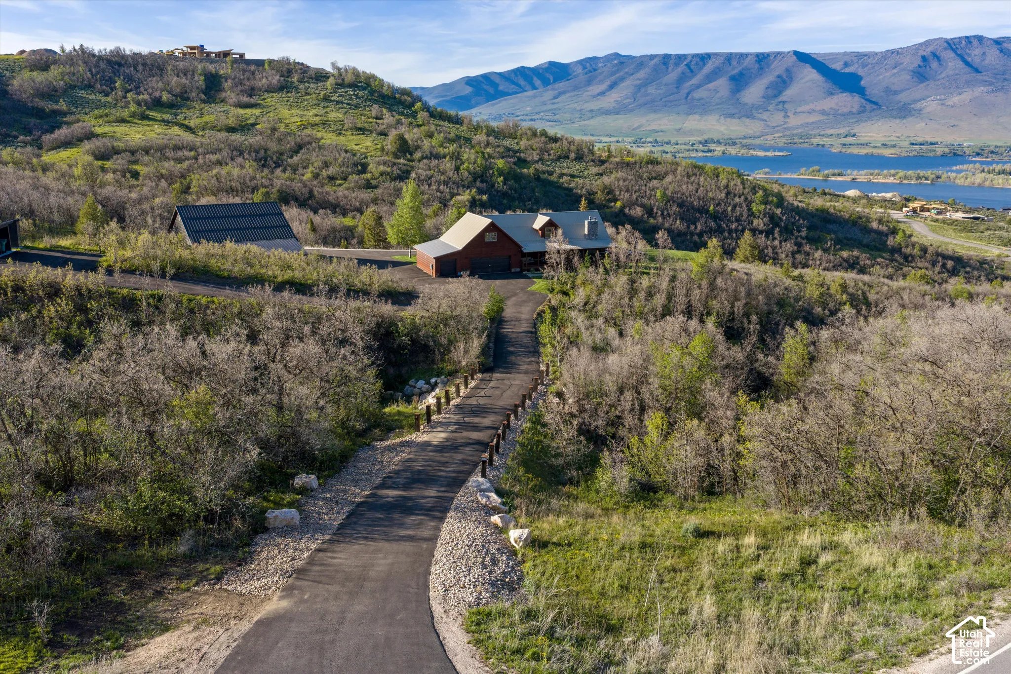 Paved driveway ascending to a secluded property, featuring a home with a prominent chimney and an additional outbuilding