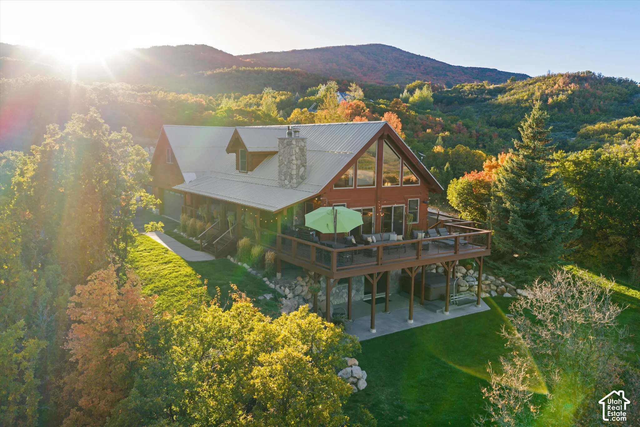 Mountain-style residence featuring a prominent A-frame window design, a large wrap-around deck, and a stone-clad chimney