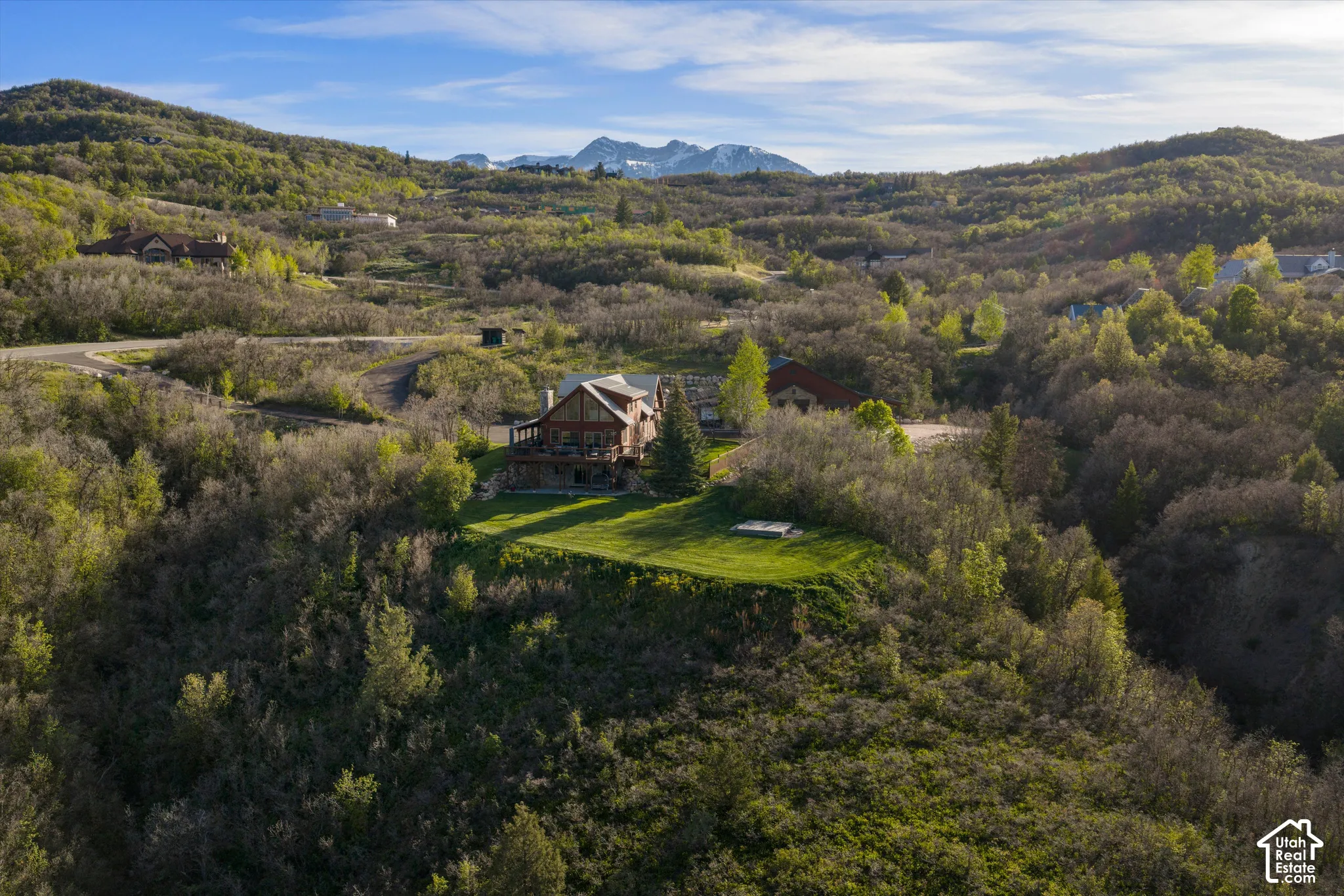 Wood-sided home with multiple exterior levels, a prominent deck, and a manicured lawn area, situated among varied natural foliage