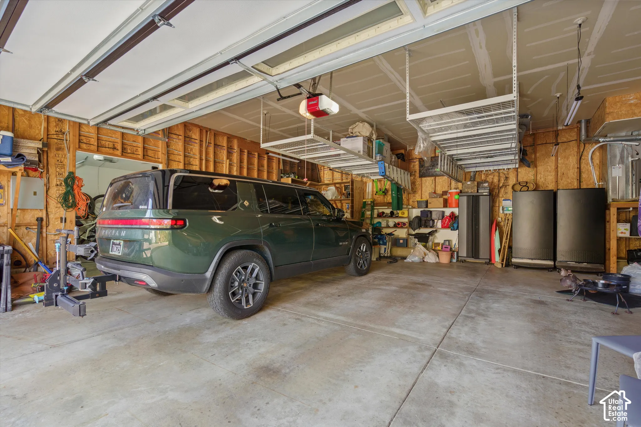 Concrete flooring, exposed wood framing, overhead storage racks, garage door opener, and fluorescent lighting