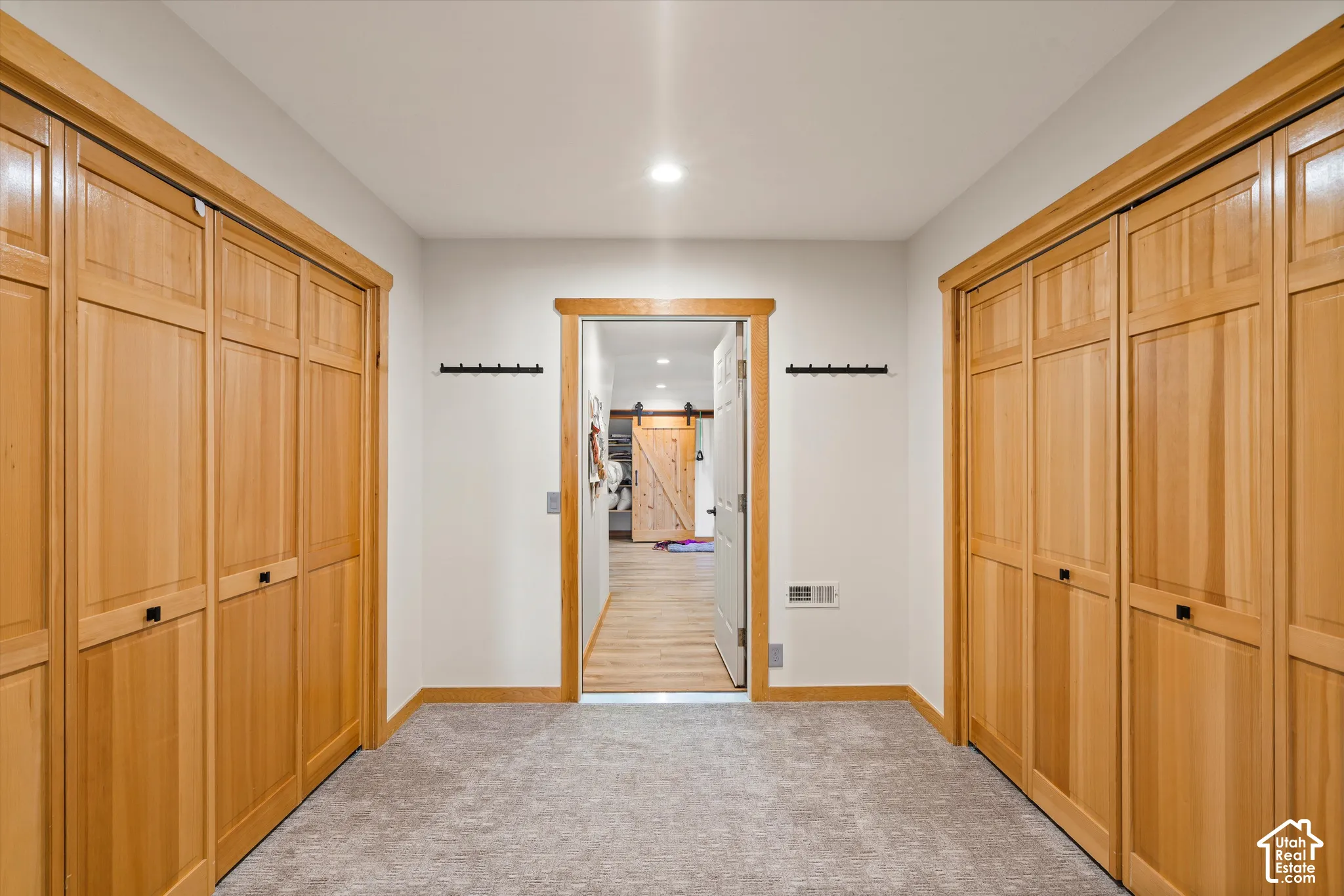 Recessed lighting illuminates the hallway with light wood-finish trim, panel doors, and gray carpeting