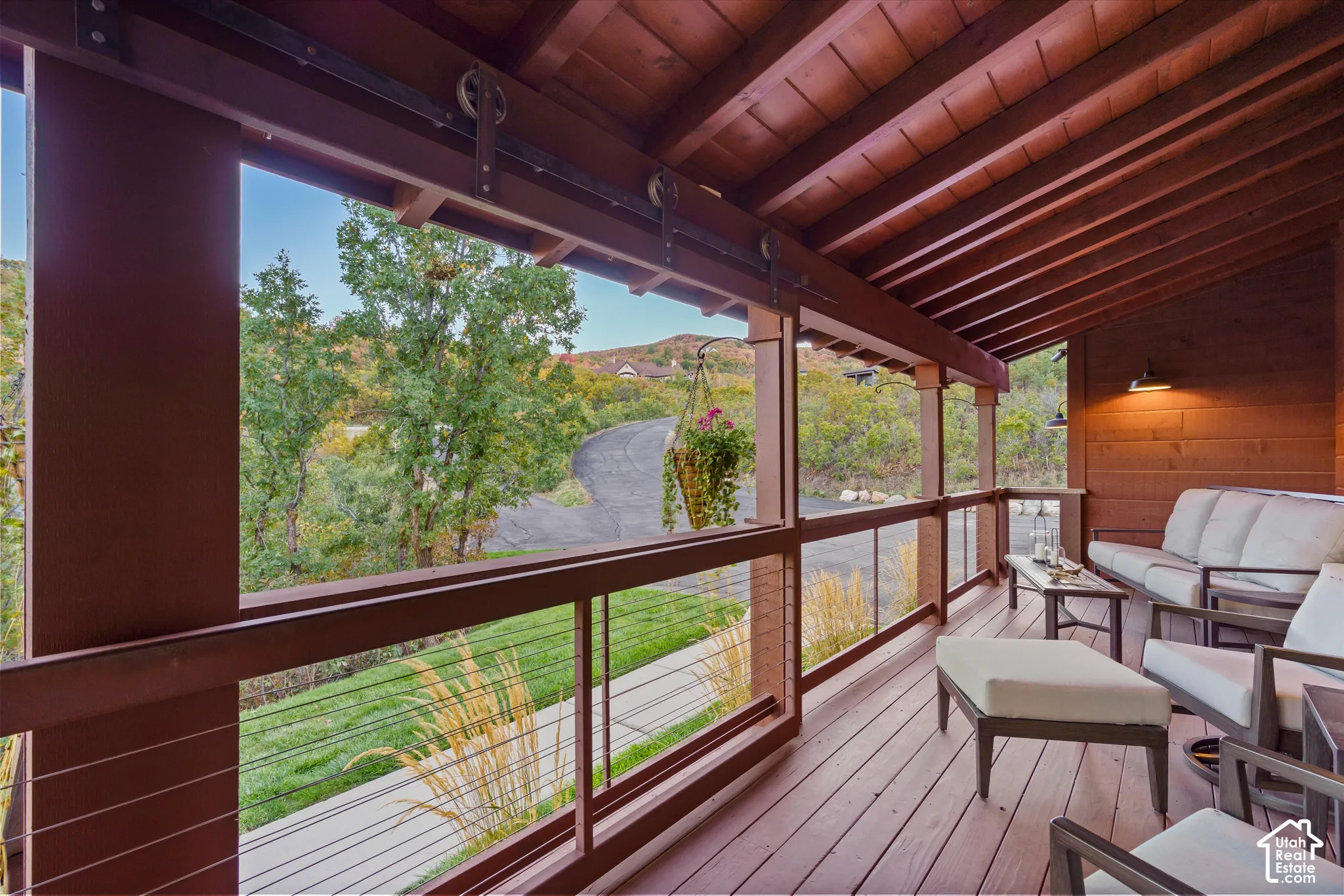 Covered outdoor deck with exposed wood beam ceiling, wood-finish flooring, and cable railing system
