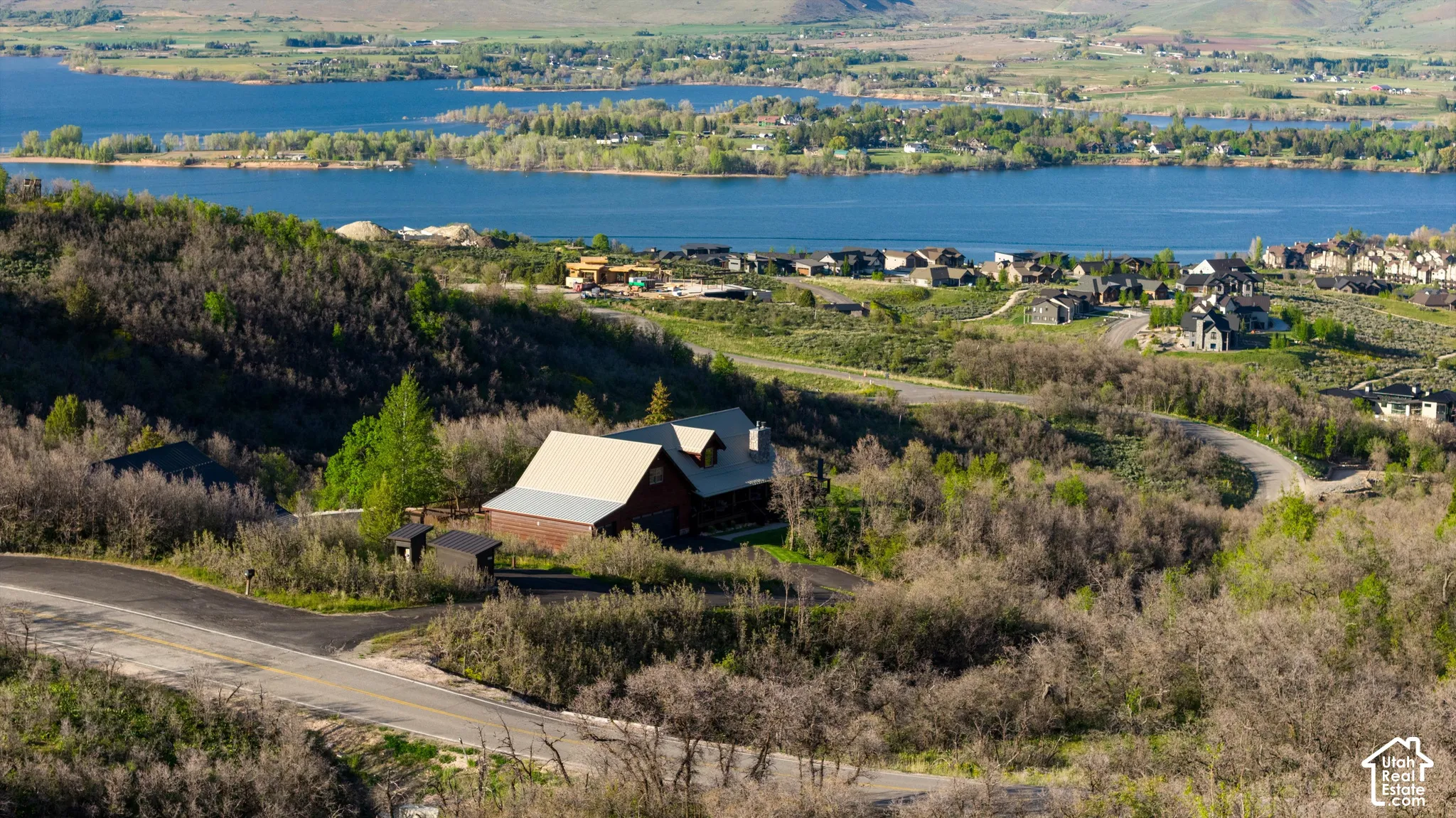 Rural setting with a barn-style structure, surrounded by natural vegetation and winding roads, with a prominent body of water in the background