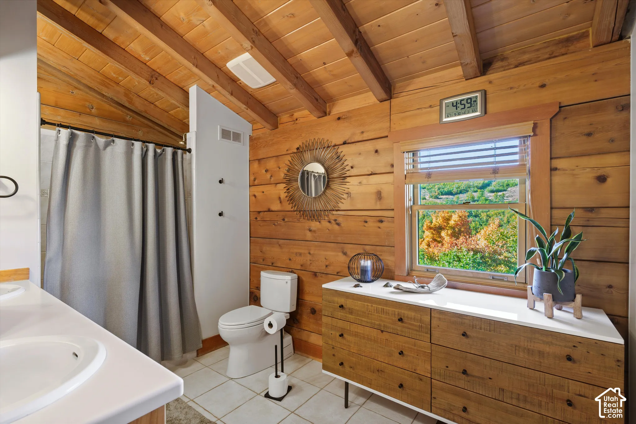 Exposed wood beam ceiling, wood-paneled walls, white tile flooring, built-in vanity with a white countertop, and a window with natural light