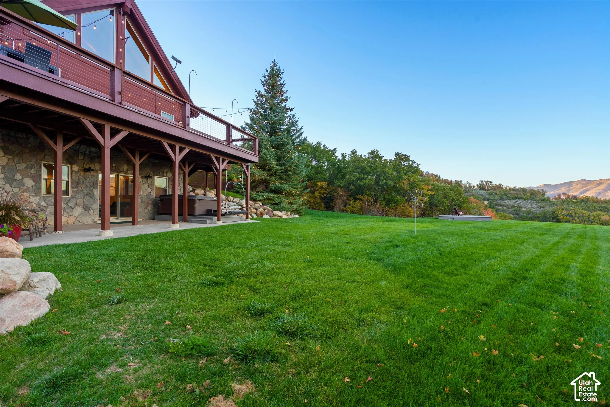 Stone exterior with a full-length covered patio, expansive lawn, and mature trees