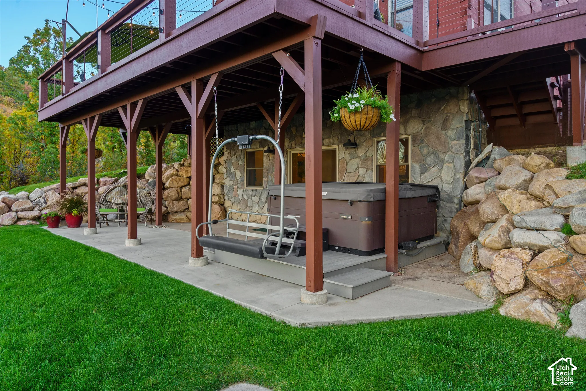 Lower-level patio with a hot tub, stone-clad exterior, and a suspended swing