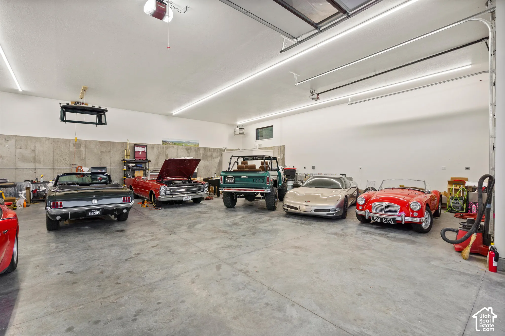 Expansive garage with concrete flooring, multiple overhead garage doors, high ceilings, and fluorescent lighting