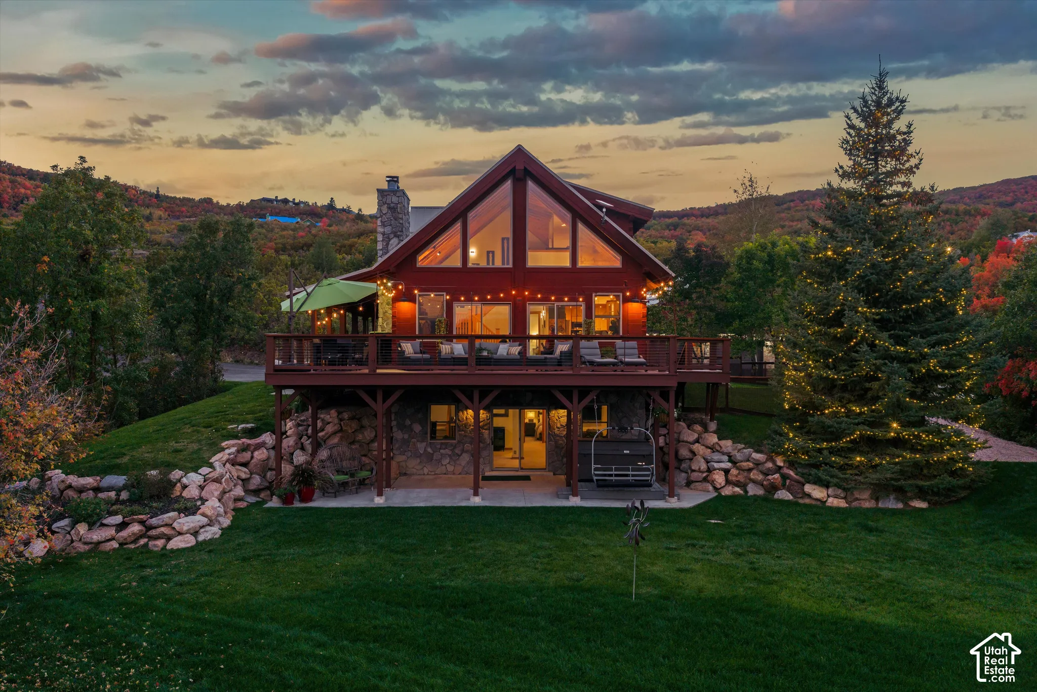 A-frame structure with expansive glass, multi-level decking, stone foundation, and a landscaped rock wall