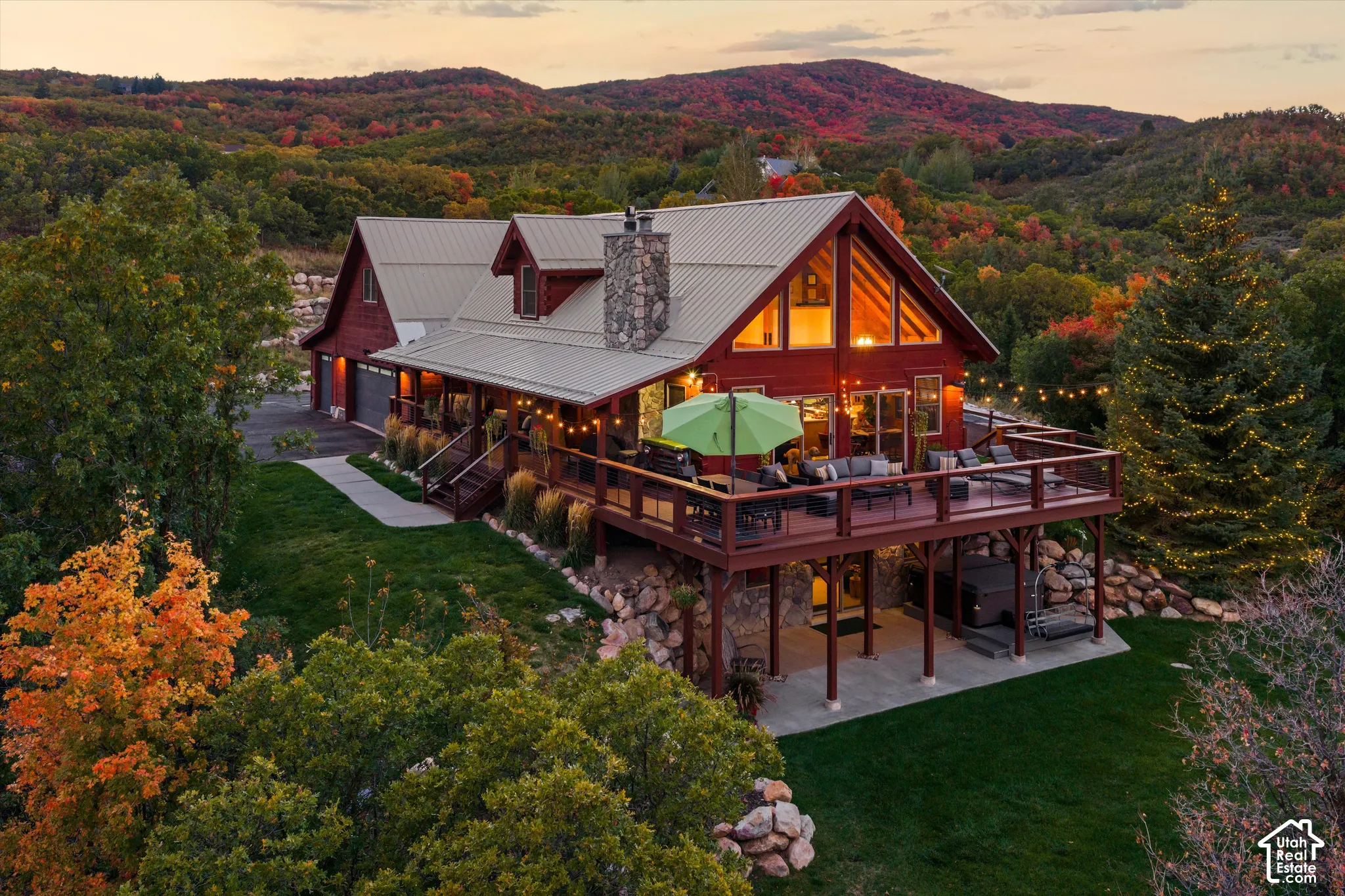 Red siding residence with an expansive elevated deck, A-frame architectural style, a stone chimney, and a detached two-car garage