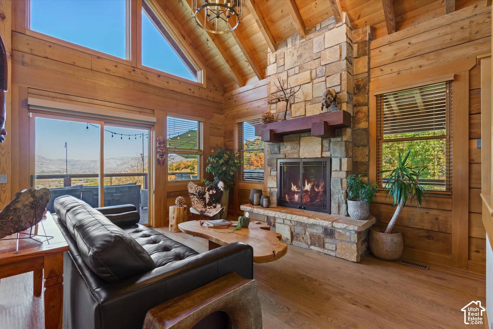Vaulted wood-paneled ceiling with exposed beams, stone-clad fireplace with hearth and mantel, wood-finish flooring, sliding glass door, and clerestory windows