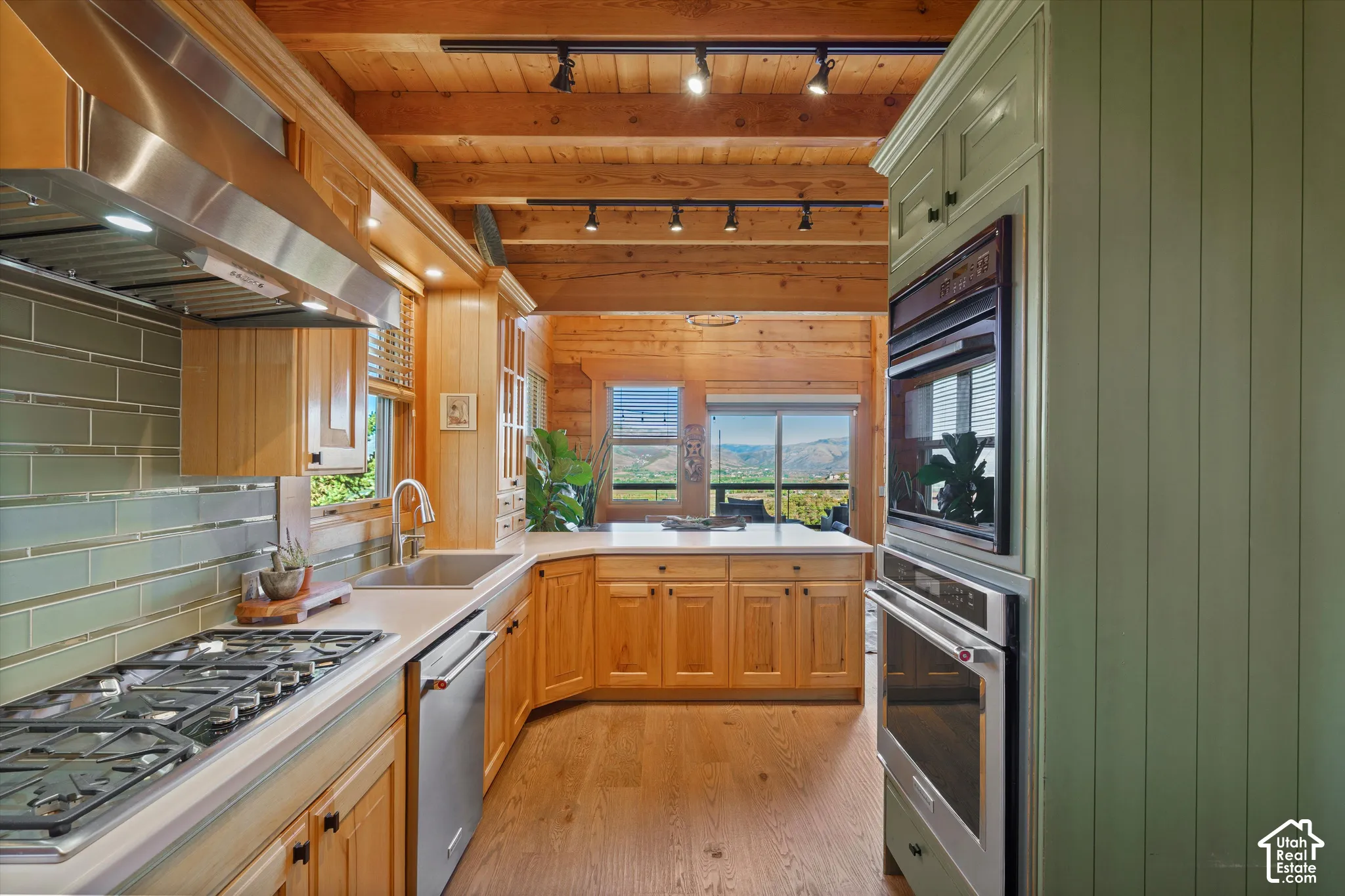 Kitchen with wood-finish flooring, wood cabinetry, light countertops, subway tile backsplash, and stainless steel appliances