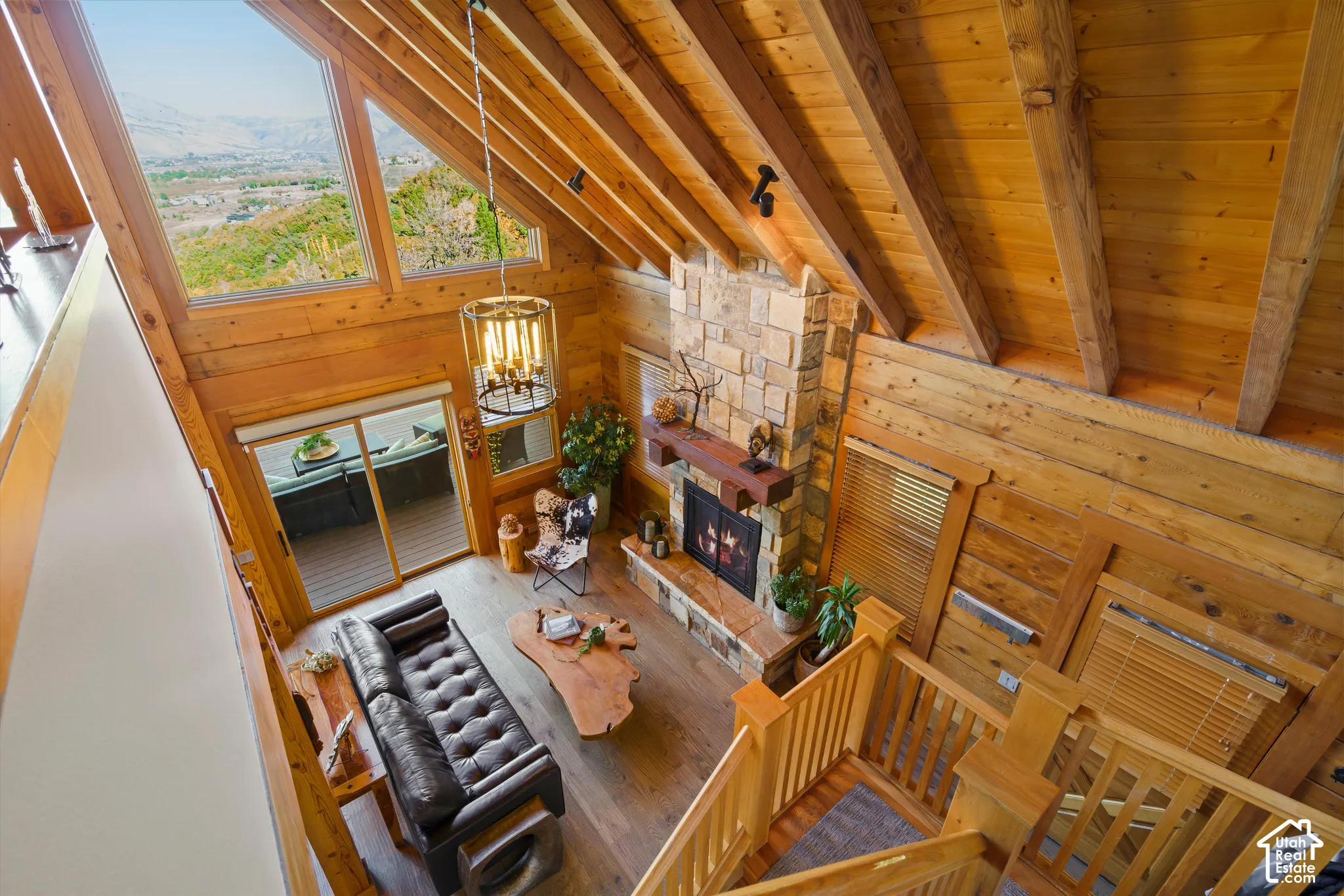 Vaulted wood-paneled ceilings with exposed beams, stone fireplace with wood mantel, wood-finish flooring, and large windows