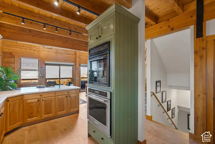 Built-in stainless steel appliances, wood-finish flooring, exposed wood beam ceiling, white countertops, and wood cabinetry