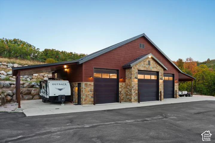 Expansive garage structure featuring multiple overhead doors, stone accents, a covered parking area, and a durable asphalt driveway
