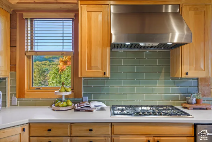 Full gas range with a stainless steel range hood, light wood cabinetry, stone countertops, and a green subway tile backsplash