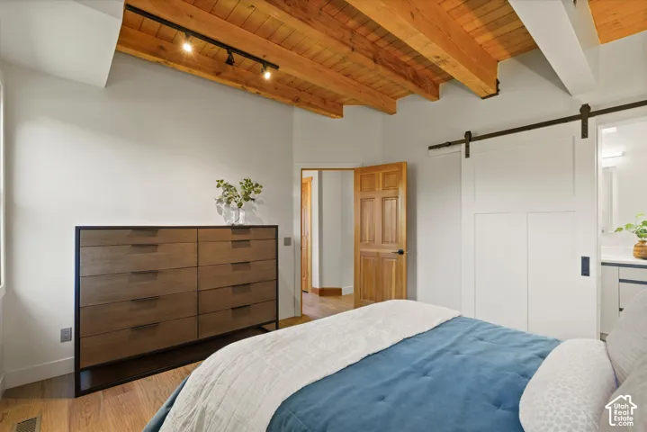 Vaulted wood-finish ceiling with exposed beams, wood-finish flooring, and a modern sliding barn door
