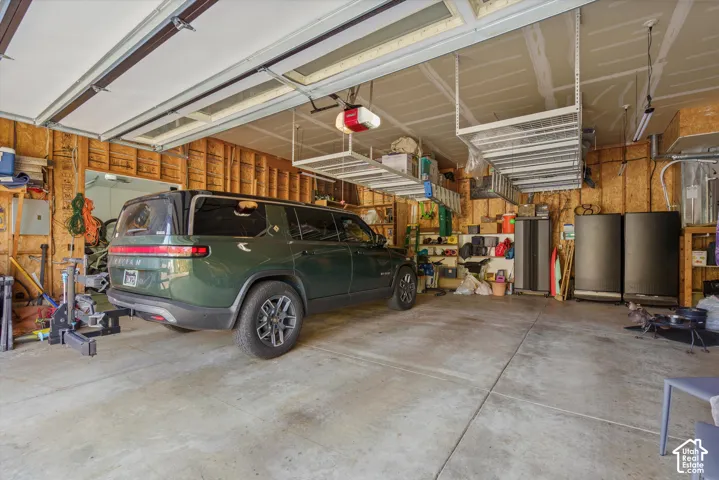 Concrete flooring, exposed wood framing, overhead storage racks, garage door opener, and fluorescent lighting
