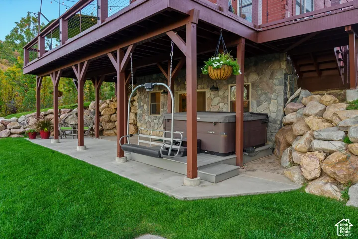 Lower-level patio with a hot tub, stone-clad exterior, and a suspended swing