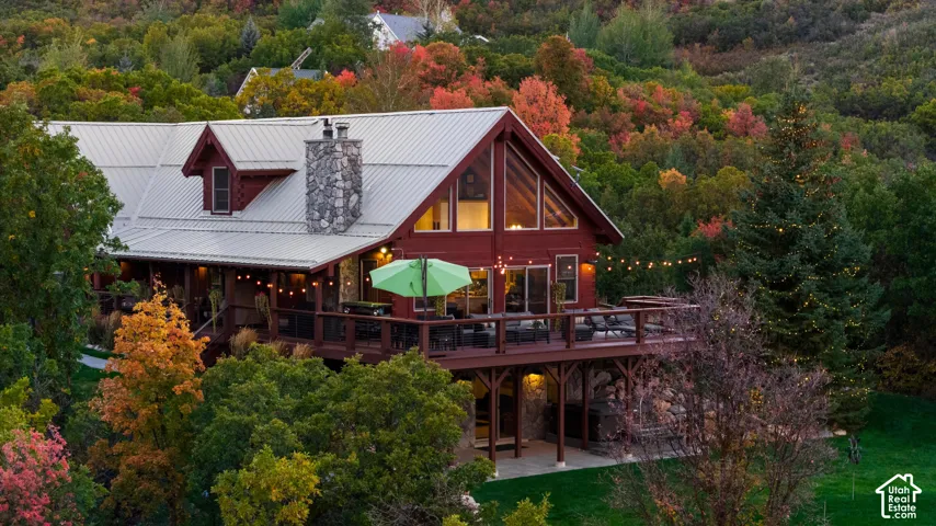 Red-sided home with a metal roof, prominent stone chimney, and a multi-level deck
