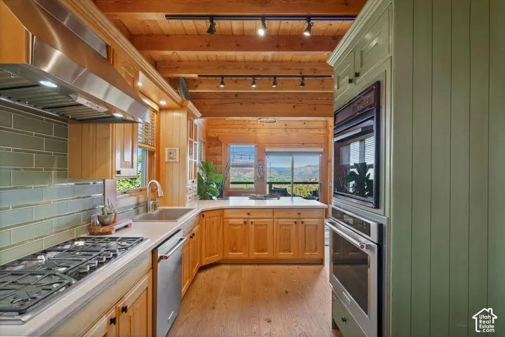 Kitchen with wood-finish flooring, wood cabinetry, light countertops, subway tile backsplash, and stainless steel appliances