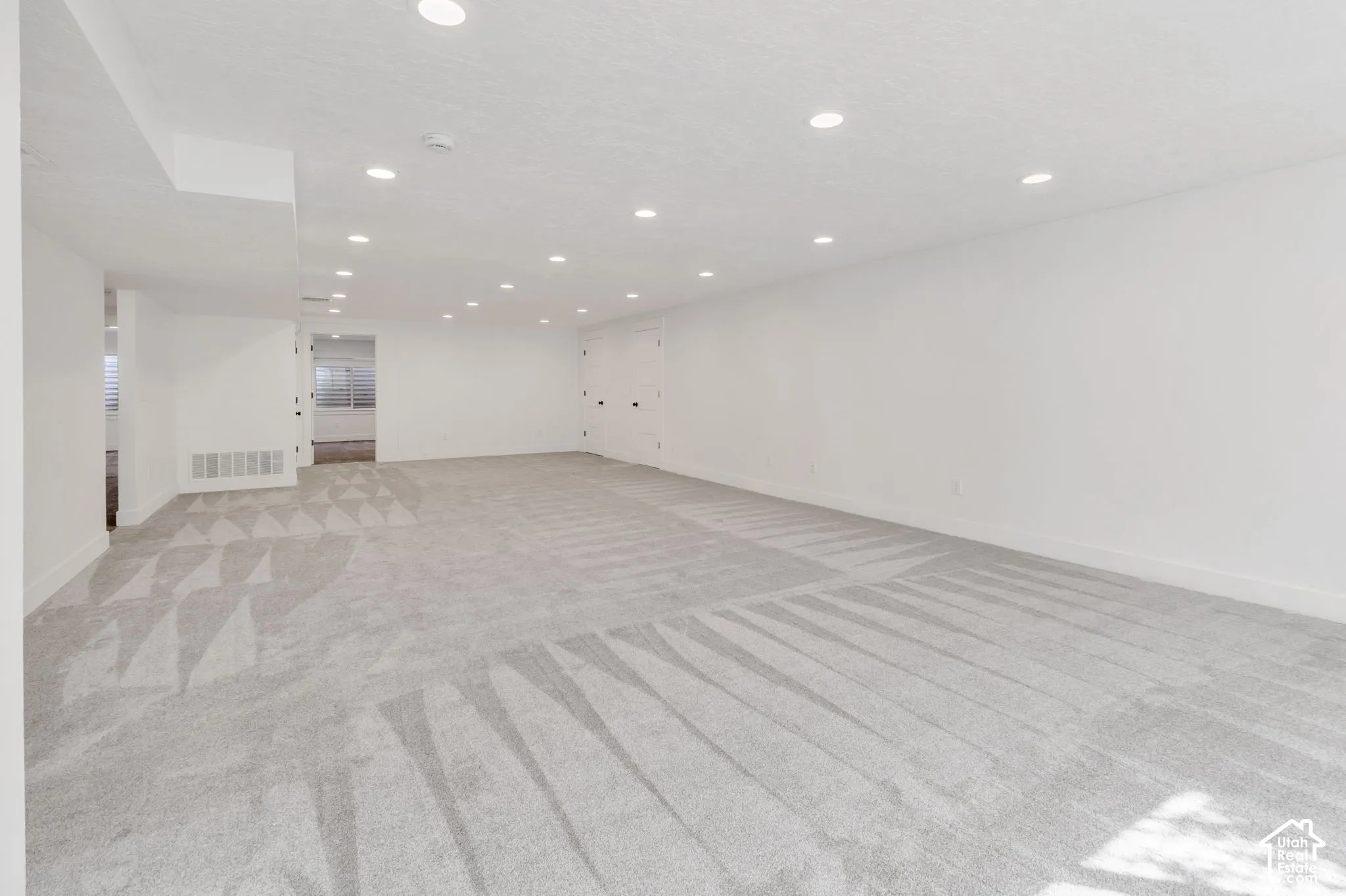 Expansive room featuring light gray carpet, recessed lighting, and white painted walls