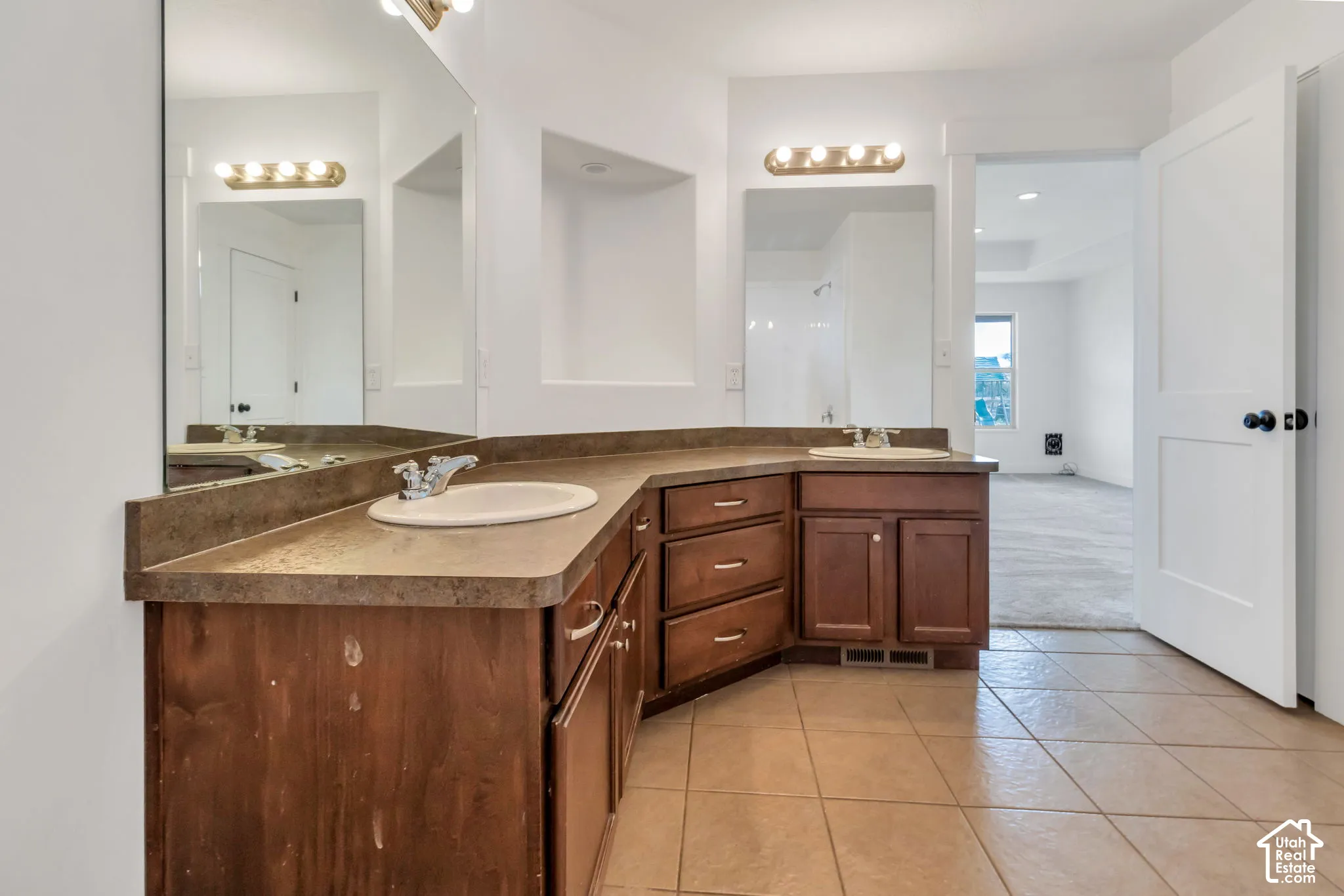 Dual vanities with integrated sinks, ample counter space, custom wood-finish cabinetry, and ceramic tile flooring