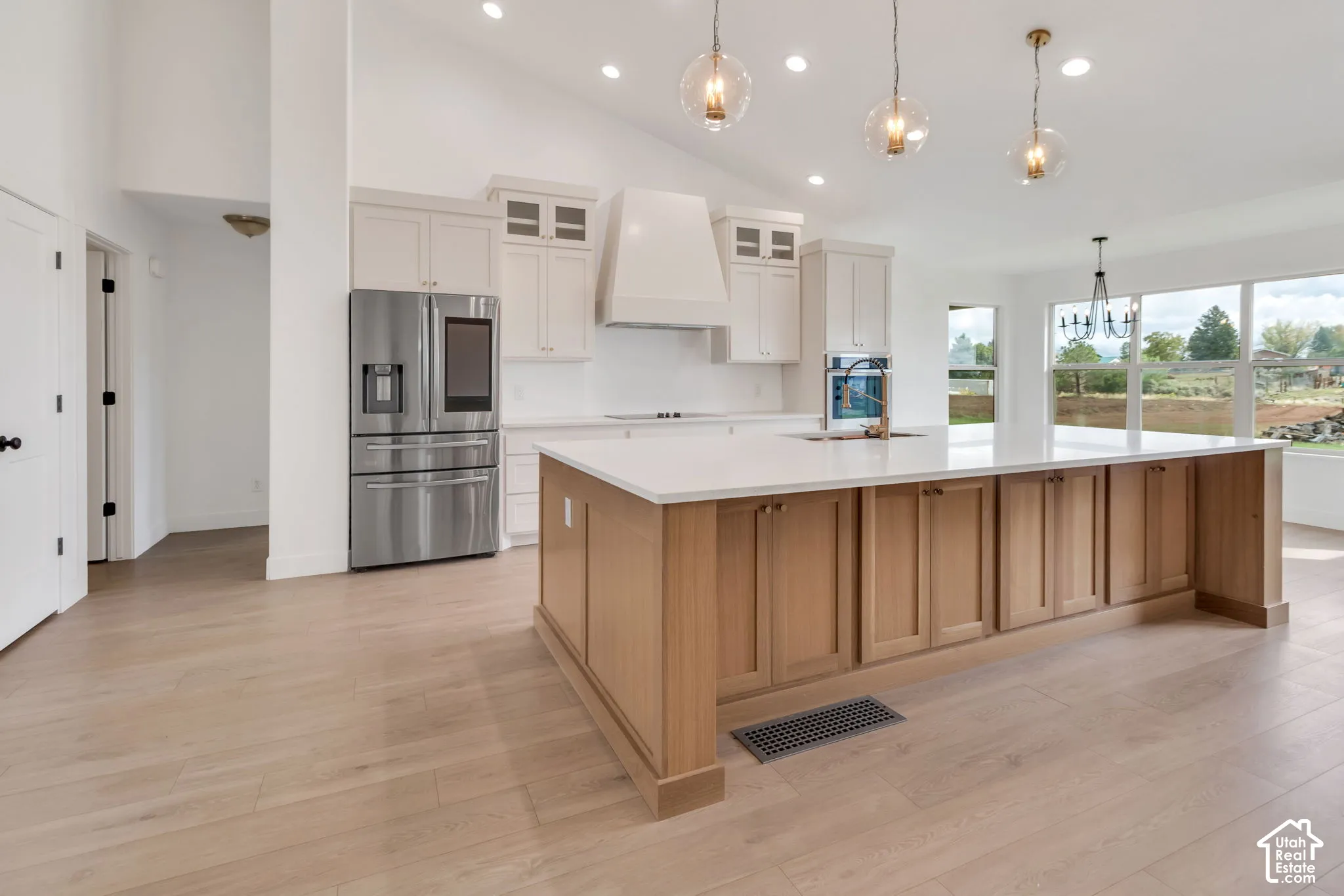 Vaulted ceiling kitchen featuring a large central island, light wood-finish flooring, recessed lighting, and stainless steel appliances