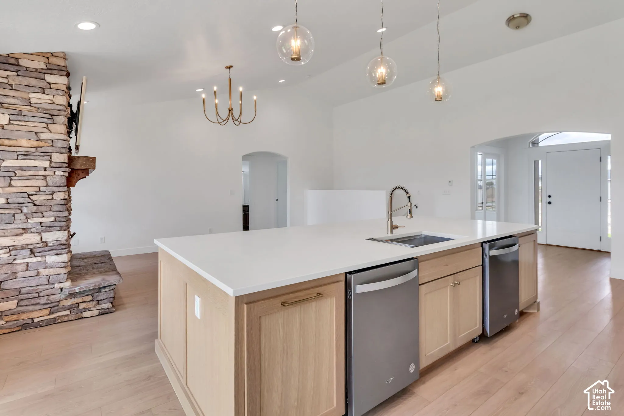 Open-concept living area featuring a stone fireplace, wood-finish flooring, and a kitchen island with built-in appliances