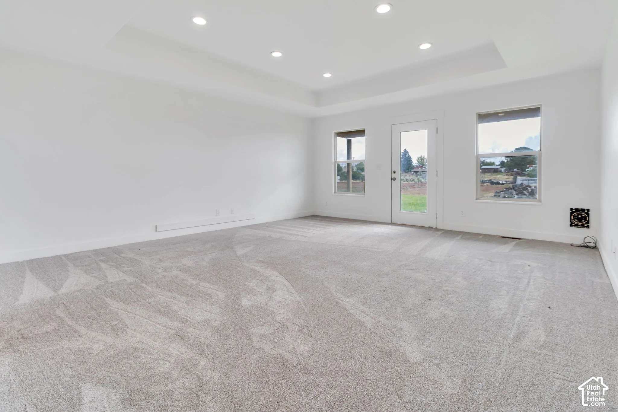 Recessed lighting illuminates a tray ceiling and light-toned carpeting