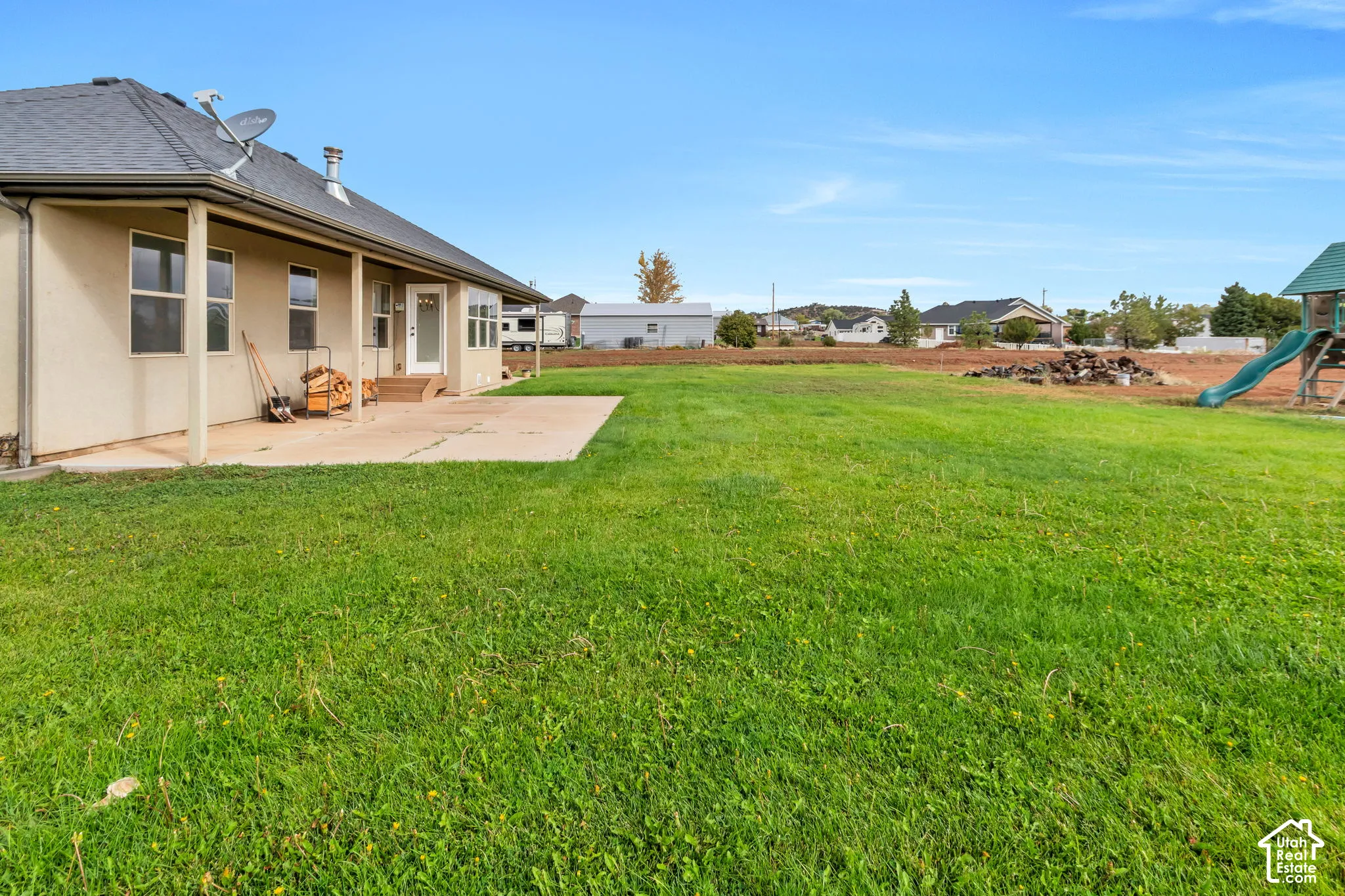 Expansive manicured lawn with mature landscaping, concrete patio, and single-story residence featuring a covered entry portico