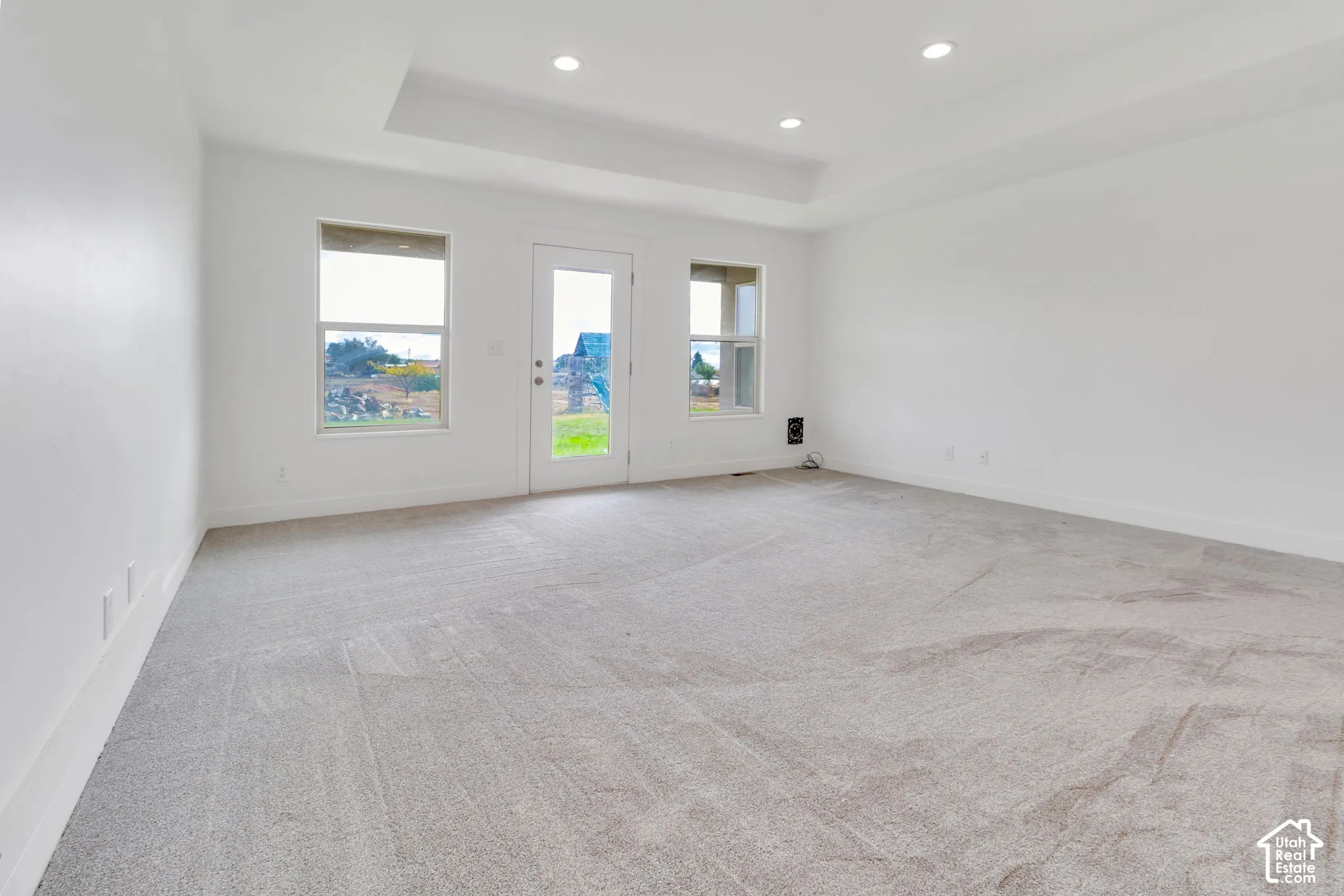 Tray ceiling with recessed lighting, light gray carpeting, white walls, and a glass-paneled exterior door