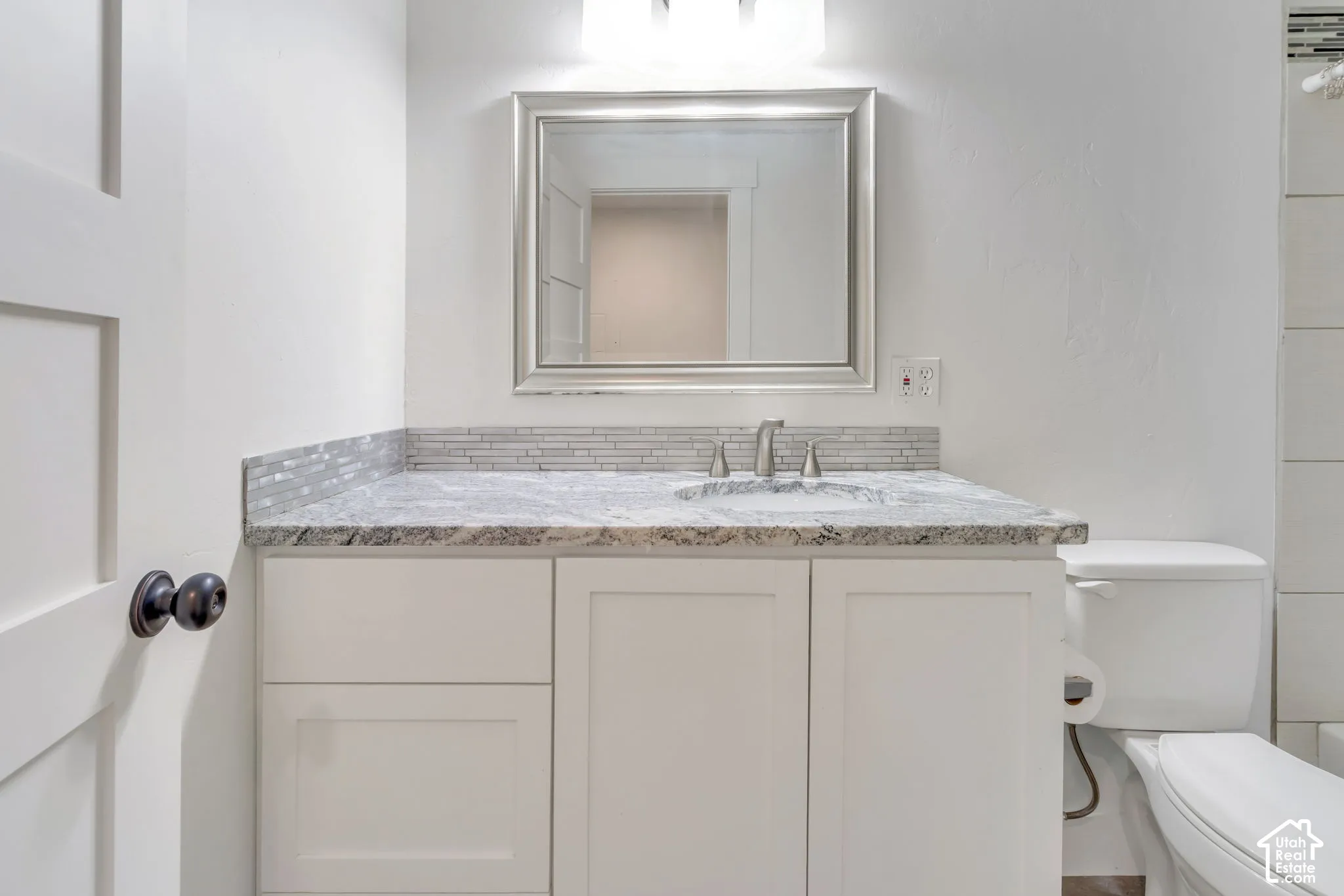 White shaker-style vanity with a light-toned countertop, mosaic tile backsplash, and a framed mirror