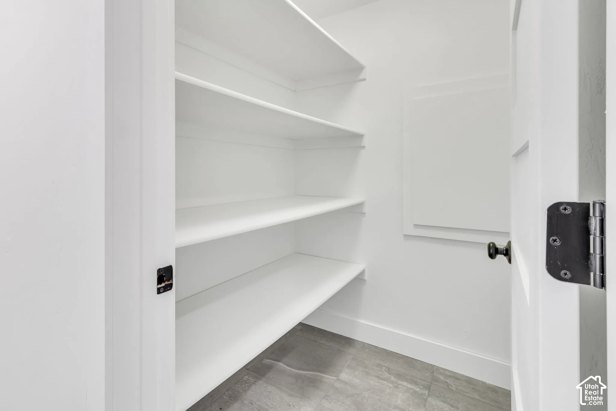 White interior featuring multiple built-in shelves, gray tile flooring, and a white panel door with black hardware