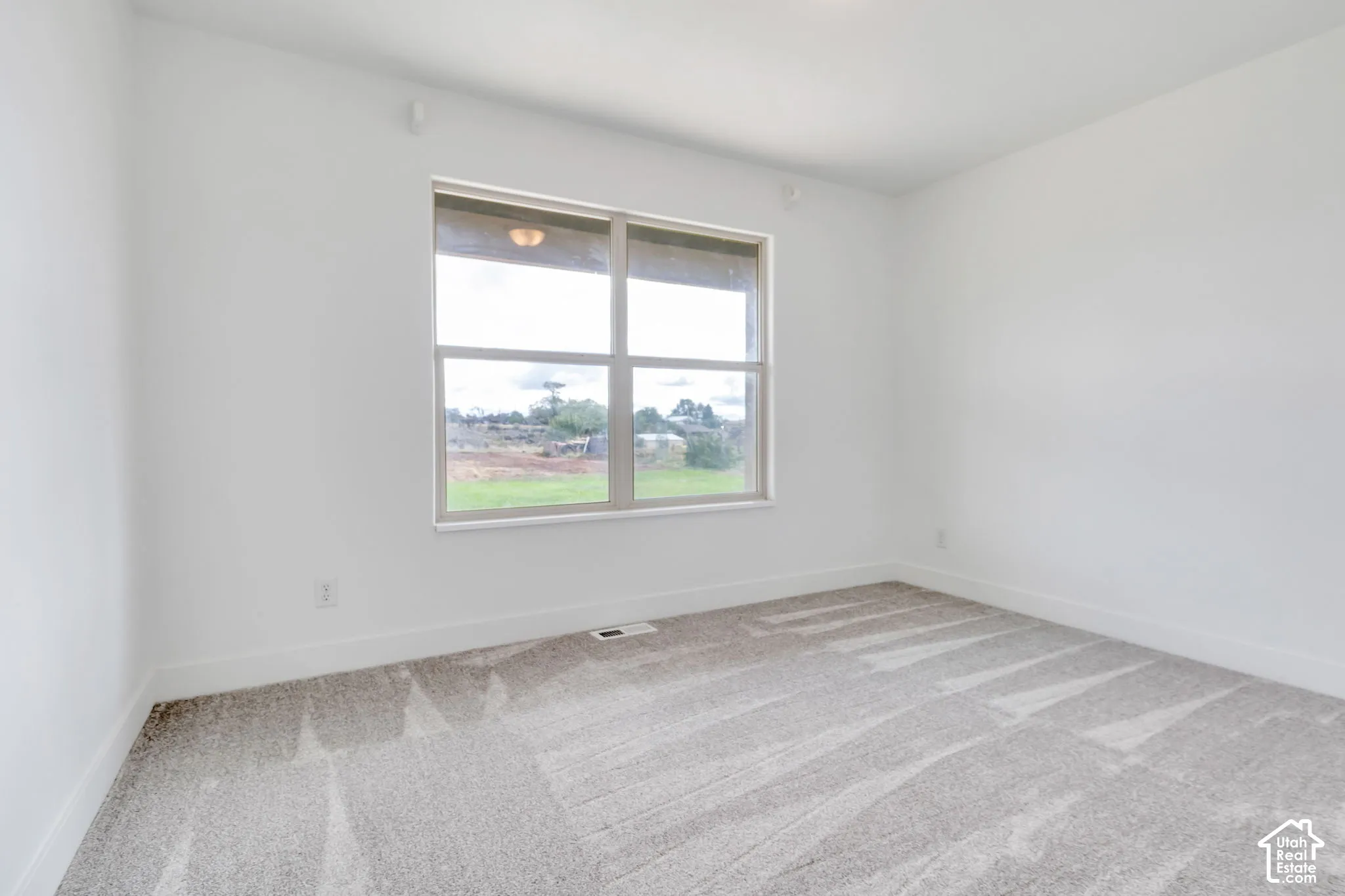 Neutral wall paint, window with white trim, and gray patterned carpeting