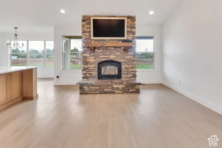 Stone-clad fireplace with a wood mantel, light wood-finish flooring, white walls, recessed lighting, and large windows