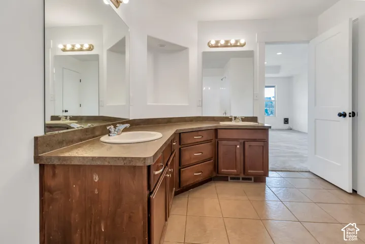 Dual vanities with integrated sinks, ample counter space, custom wood-finish cabinetry, and ceramic tile flooring