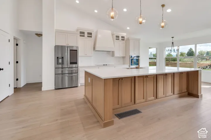 Vaulted ceiling kitchen featuring a large central island, light wood-finish flooring, recessed lighting, and stainless steel appliances