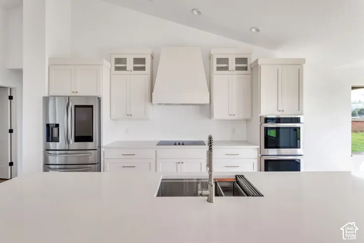White shaker cabinetry, stainless steel appliances, built-in double ovens, large kitchen island with integrated sink, and a cooktop