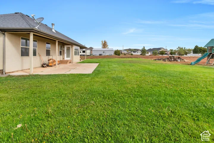 Expansive manicured lawn with mature landscaping, concrete patio, and single-story residence featuring a covered entry portico