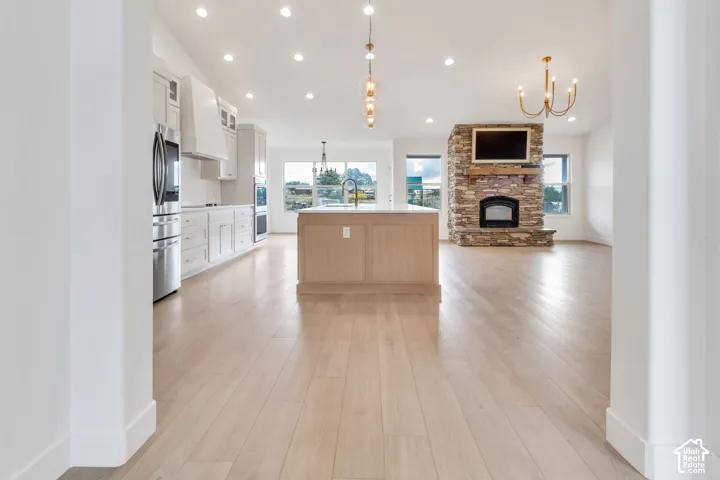 Open-concept living space with light wood-finish flooring, a stone-clad fireplace, and recessed lighting