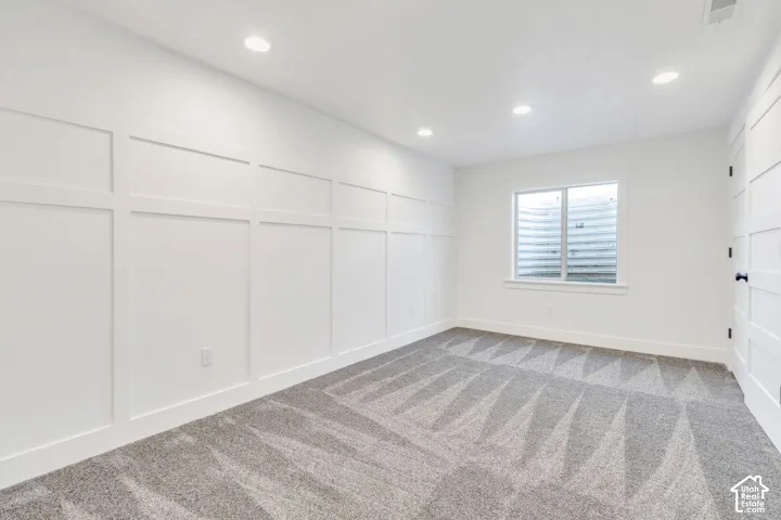 Board and batten accent wall, recessed ceiling lighting, carpeted flooring, window with white trim, and a paneled door with dark hardware
